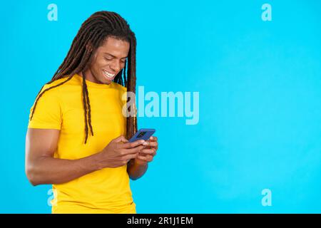 Happy latin man with dreadlocks smiling while using the mobile Stock Photo