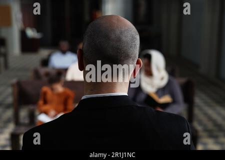 Rear view of protestant in black suit reading Bible for believers while they sitting on bench in baptist church Stock Photo