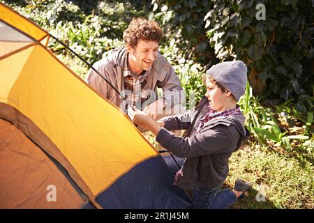 Father, child and smile while set up tent for camping outdoor in nature on vacation, bonding together and summer. Dad, boy and preparing camp Stock Photo