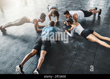 The comfort zone has no place in a gym. a group of young people doing planks together during their workout in a gym. Stock Photo