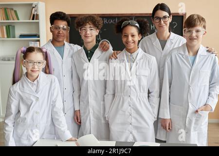 Diverse group of happy teenagers wearing lab coats in school and looking at camera posing together Stock Photo