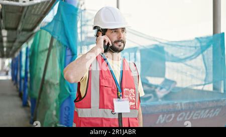 Young hispanic man builder talking on smartphone standing at street Stock Photo