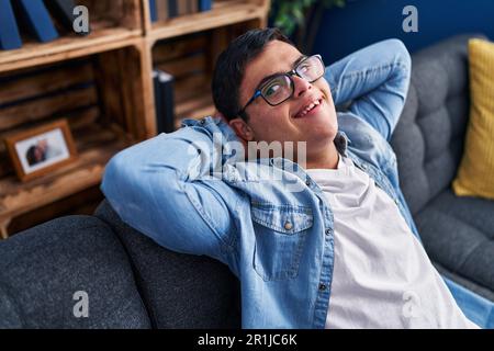 Down syndrome man relaxed with hands on head sitting on sofa at home Stock Photo
