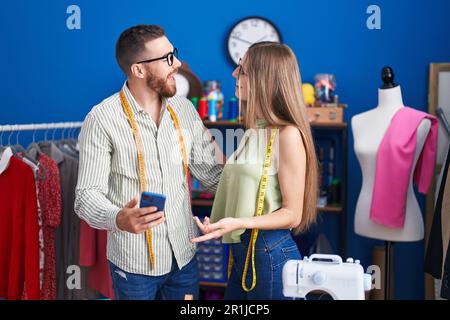 Man and woman tailors smiling confident using smartphone at clothing factory Stock Photo