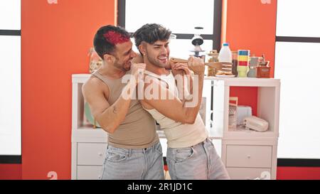 Two men couple singing song using kitchen utensil as a microphone at dinning room Stock Photo