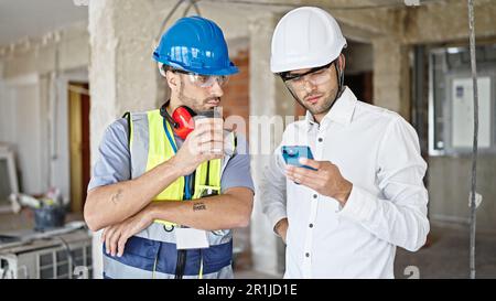 Two men builders and architect using smartphone drinking coffee at construction site Stock Photo