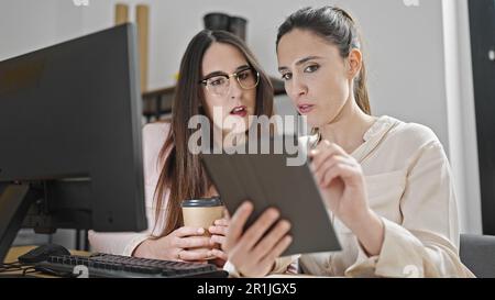 Two women business workers using touchpad drinking coffee at office Stock Photo