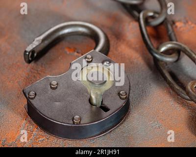 Open padlock with key and an old rusty link chain on a grunge orange background Stock Photo