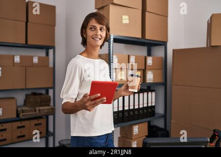Young beautiful hispanic woman ecommerce business worker using touchpad drinking coffee at office Stock Photo