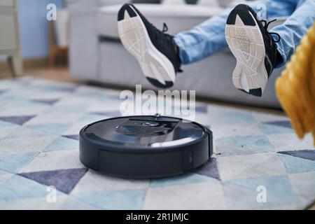 African american man cleaning rug using robot vacuum cleaner at home Stock Photo