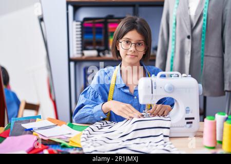 Adorable hispanic girl tailor smiling confident using sewing machine at clothing factory Stock Photo