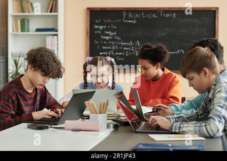 Diverse group of teen children using laptops in school classroom and studying together Stock Photo