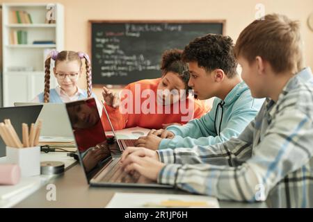 Diverse group of children using laptops in school classroom with black girl peeking at computer screen Stock Photo
