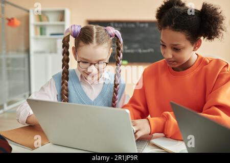 Portrait of two teen schoolgirls using laptop together in classroom looking at computer screen Stock Photo