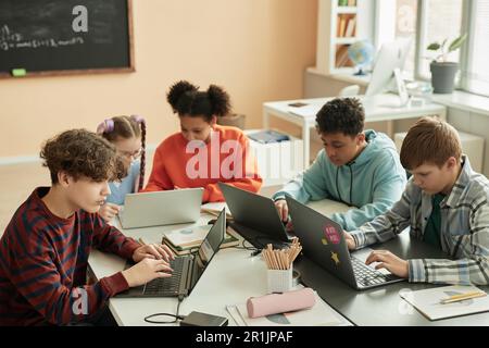 High angle view at diverse group of teen schoolchildren using computers in classroom studying together Stock Photo