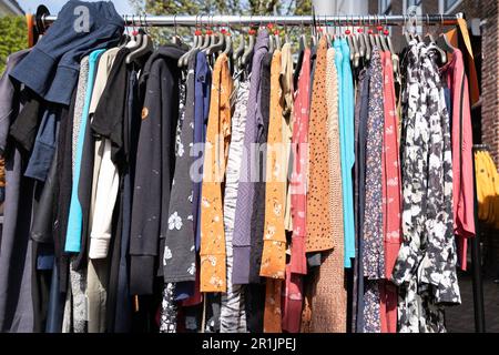 Cheap colorful summer dresses hang back to back in the sun on wooden hangers at an open-air market in the Netherlands Stock Photo