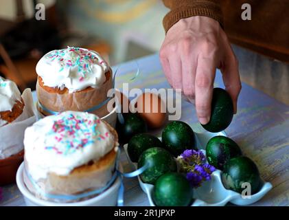 Three Easter cakes for Easter on the table. Traditional painted eggs on a stand.Man's hand holding an easter egg Stock Photo