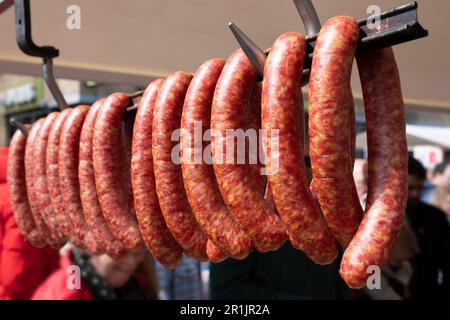 Traditionally prepared dried sausages ('rookworst') hang outside a butcher's shop on a metal bar. People walk past the display in the background Stock Photo