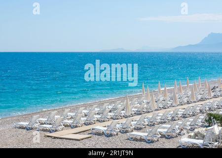 Landscape coast with white beach umbrellas and sun loungers on the sand beach, against the backdrop of grief in the distance Stock Photo
