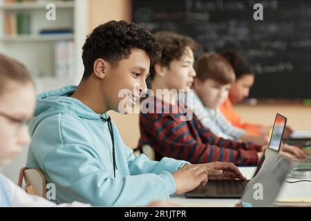 Side view at teen schoolboy using computer in row in school classroom and taking online exam Stock Photo