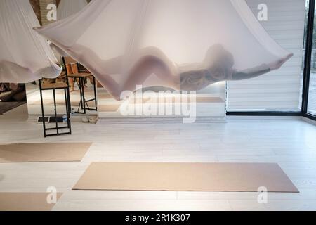 Silhouette of a lying fit shapely gracile girl completely hidden by a red hammock during relaxing moments in antigravity yoga class Stock Photo