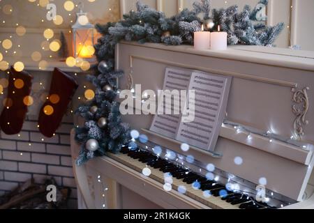 White piano with festive decor and note sheets indoors. Christmas music Stock Photo