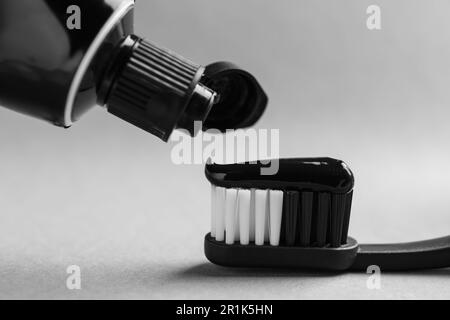 Applying charcoal toothpaste on brush against light grey background, closeup Stock Photo