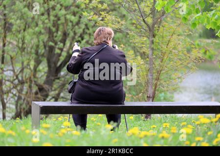 Fat woman sitting with walking canes on a bench in a park. Healthy lifestyle in old age, nordic walking Stock Photo