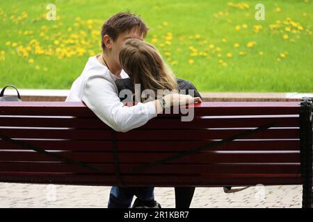 Young couple kissing on a city street. Girl and guy embracing sitting on a bench in spring park Stock Photo