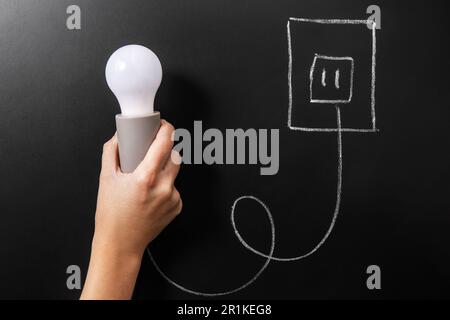 close up of hand holding lightbulb over chalkboard Stock Photo