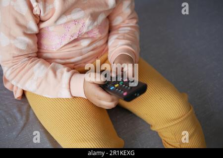 child holding a tv remote sitting on sofa  Stock Photo