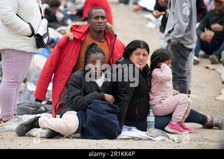 Asylum seekers sit in a line of migrants waiting to be caravanned by Border Patrol to be officially processed into the U.S. System. As Title 42 has officially expired in the United States, which was policy established during the Trump-era allowing authorities including Border Patrol to turn away migrants at the borders to prevent the ongoing Corona Virus pandemic, Asylum seekers can be seen camped between the San Diego, California border and Mexico border waiting to be processed in to United States system. Scattered with an array of nationalities, these migrants have traveled from near and far Stock Photo