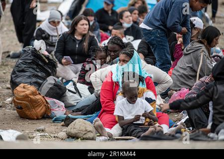 Asylum seekers sit in a line of migrants waiting to be caravanned by Border Patrol to be officially processed into the U.S. System. As Title 42 has officially expired in the United States, which was policy established during the Trump-era allowing authorities including Border Patrol to turn away migrants at the borders to prevent the ongoing Corona Virus pandemic, Asylum seekers can be seen camped between the San Diego, California border and Mexico border waiting to be processed in to United States system. Scattered with an array of nationalities, these migrants have traveled from near and far Stock Photo