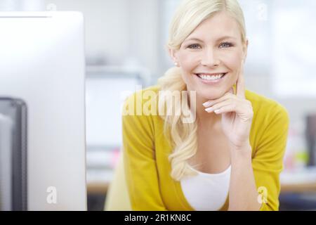 Portrait of a businesswoman sitting behind her computer at her desk and smiling while looking at the camera. One confident creative designer sitting Stock Photo