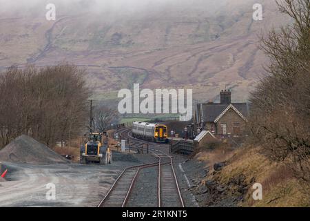Viewed from the quarry freight sidings a Northern Rail class 158 DMU train arrives at Ribblehead station on the Settle to Carlisle railway Stock Photo