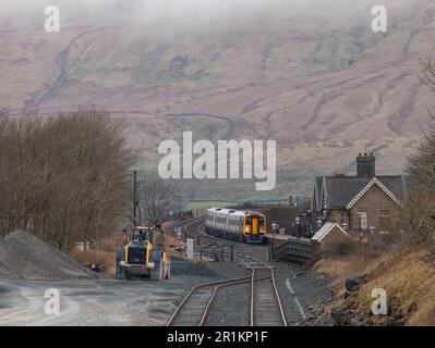 Viewed from the quarry freight sidings a Northern Rail class 158 DMU train arrives at Ribblehead station on the Settle to Carlisle railway Stock Photo