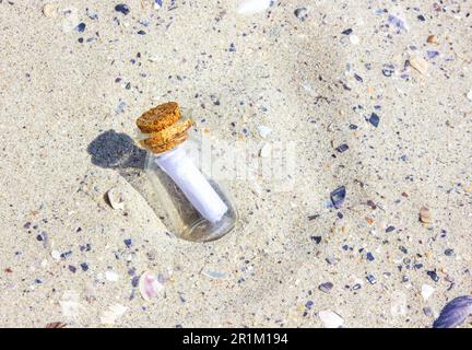 A message in a Corked Bottle on a beach. The bottle in the sand. The bottle on sandy beach. Sunny day. Stock Photo