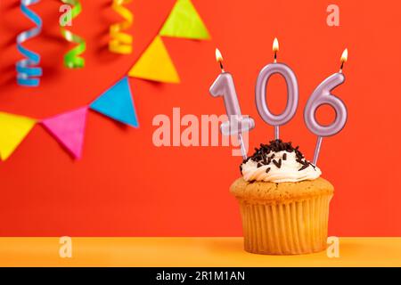 Birthday cake with number 106 candle - Sparkling orange background with bunting Stock Photo