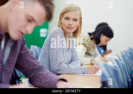 Its all about good grades. Portrait of a university student writing an exam with other students. Stock Photo