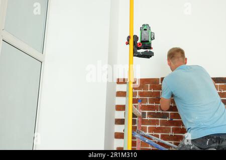 Professional builder using cross line laser level while gluing decorative bricks on wall, back view. Tiles installation process Stock Photo