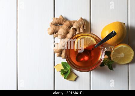 Cup of delicious tea, ginger roots and lemons on white wooden table, flat lay. Space for text Stock Photo