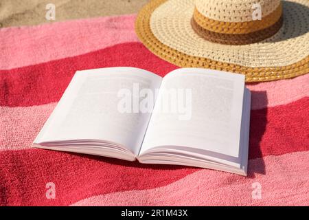 Open book, hat and striped towel on sandy beach Stock Photo