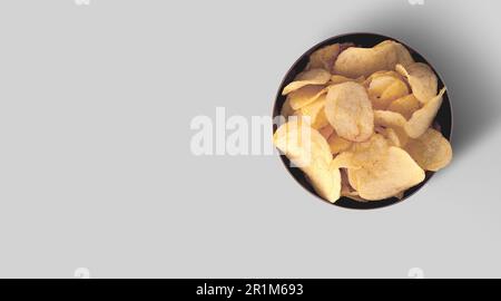 Crispy potato chips in a black ceramic tray on a grey background, top view. Stock Photo