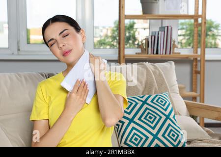 Young woman using heating pad on neck at home Stock Photo