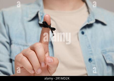Man showing index finger with tied bow as reminder against light grey background, focus on hand Stock Photo