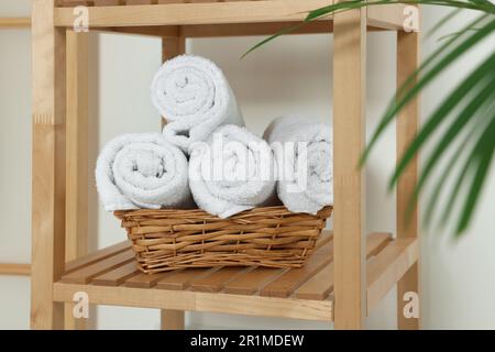Soft folded towels in wicker basket on wooden shelving unit Stock Photo