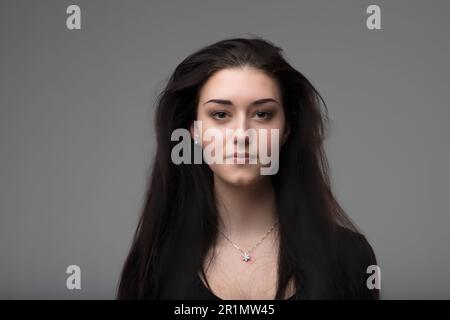 Frontal portrait of serious, elegant young woman with black eyes and long black hair, intense and intelligent gaze, proud Italian, aware of her beauty Stock Photo