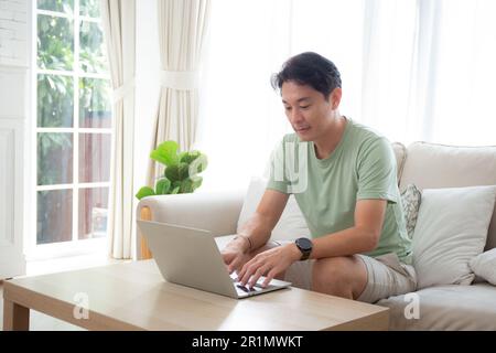 Young asian man typing keyboard on laptop computer on desk at home, businessman working to internet online, freelance male using notebook on table, co Stock Photo