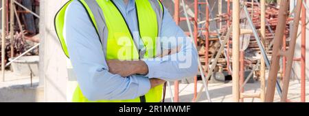 Portrait of young man is engineer wearing helmet smile with satisfied at construction site, architect or contractor standing and arms crossed with con Stock Photo