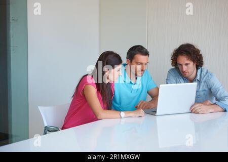 Putting their heads together. three coworkers gathered around a laptop in the office. Stock Photo